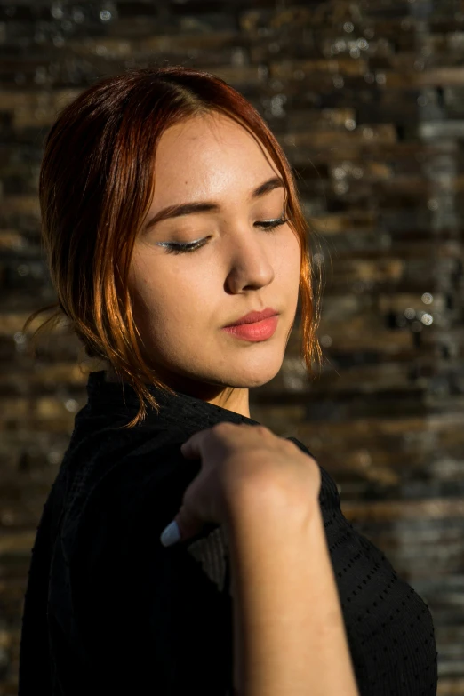 a woman standing in front of a brick wall, inspired by Elsa Bleda, trending on pexels, realism, copper hair, young asian woman, softly backlit, taken with sony alpha 9