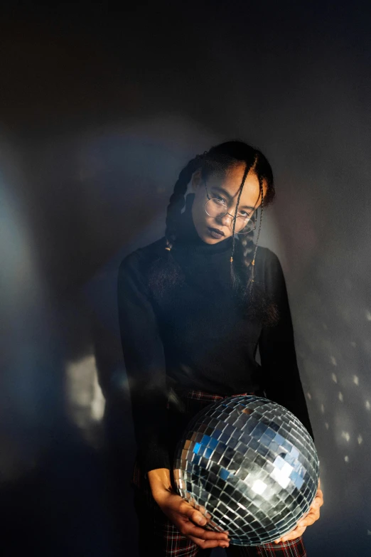 a woman holding a disco ball in her hands, an album cover, inspired by Ai-Mitsu, trending on unsplash, neo-figurative, frank dillane, asian woman, serious lighting, photograph of a techwear woman