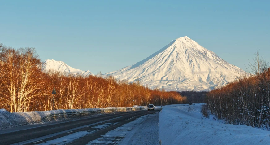 a car driving down a snowy road with a mountain in the background, inspired by Illarion Pryanishnikov, pexels contest winner, hurufiyya, infographic of active volcanoes, in an arctic forest, russian and japanese mix, taken in the late 2010s