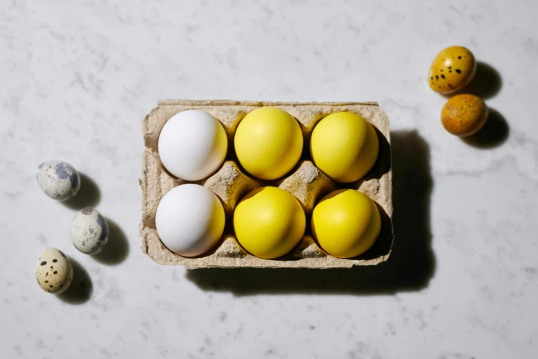 a carton filled with eggs sitting on top of a table, with a bright yellow aureola, bright white porcelain, varying ethnicities, 6 pack