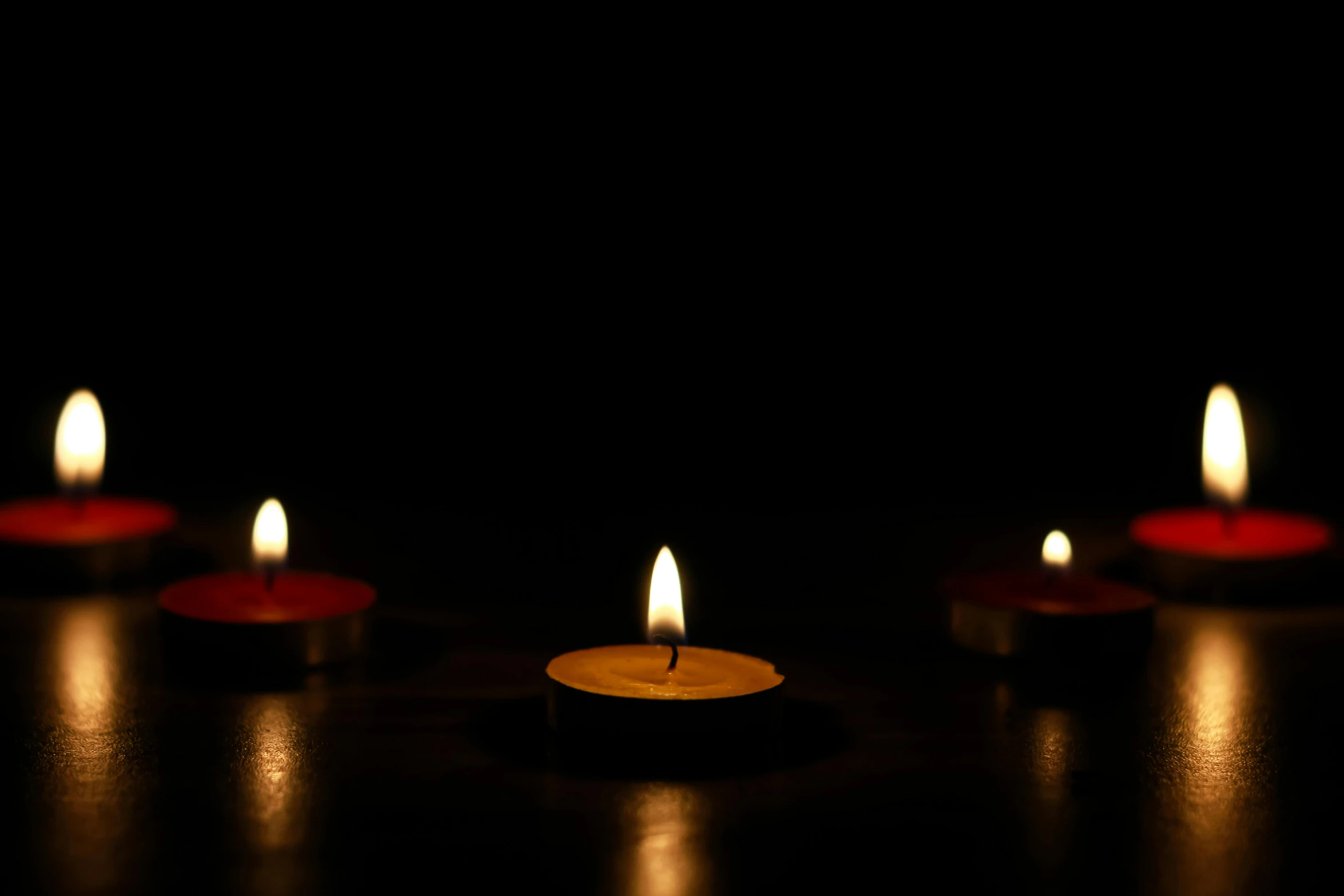 a group of lit candles sitting on top of a table, with a black background, photograph of april, glowing red, distant photo