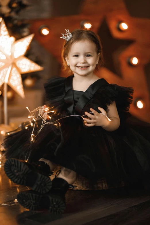 a little girl sitting in front of a christmas tree, a portrait, by Julia Pishtar, pexels contest winner, shiny black dress, happy birthday, 15081959 21121991 01012000 4k, modern stylish glamour tutu