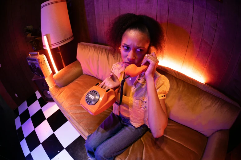 a woman sitting on a couch talking on a phone, by Anson Maddocks, pexels, conceptual art, orange lighting, wax figure, ashteroth, todd solondz