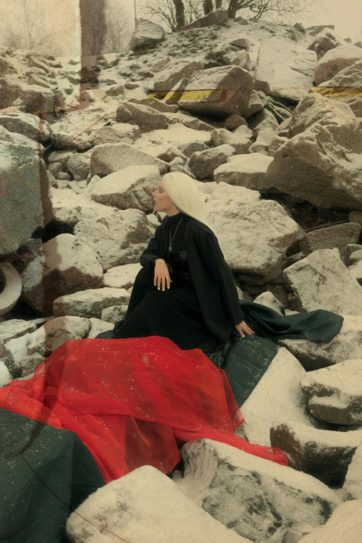 a woman laying on top of a pile of rocks, an album cover, by Elsa Bleda, billie eilish as a nun, brutalist fashion show, crumbled wall in jerusalem, ( ( theatrical ) )