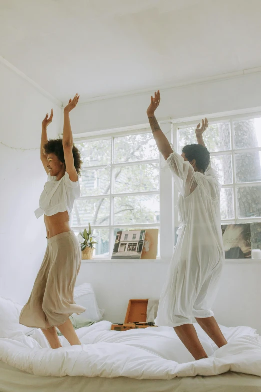 a couple of women jumping on top of a bed, by Jessie Algie, pexels contest winner, arabesque, dance meditation, in a living room, two skinny figures, hands up