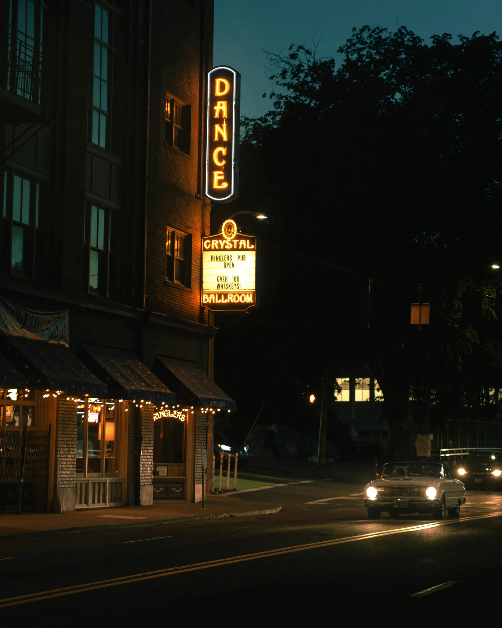 a car drives down a city street at night, an album cover, by Dan Frazier, unsplash contest winner, renaissance, stephen shore, theater, a quaint, 1987 photograph