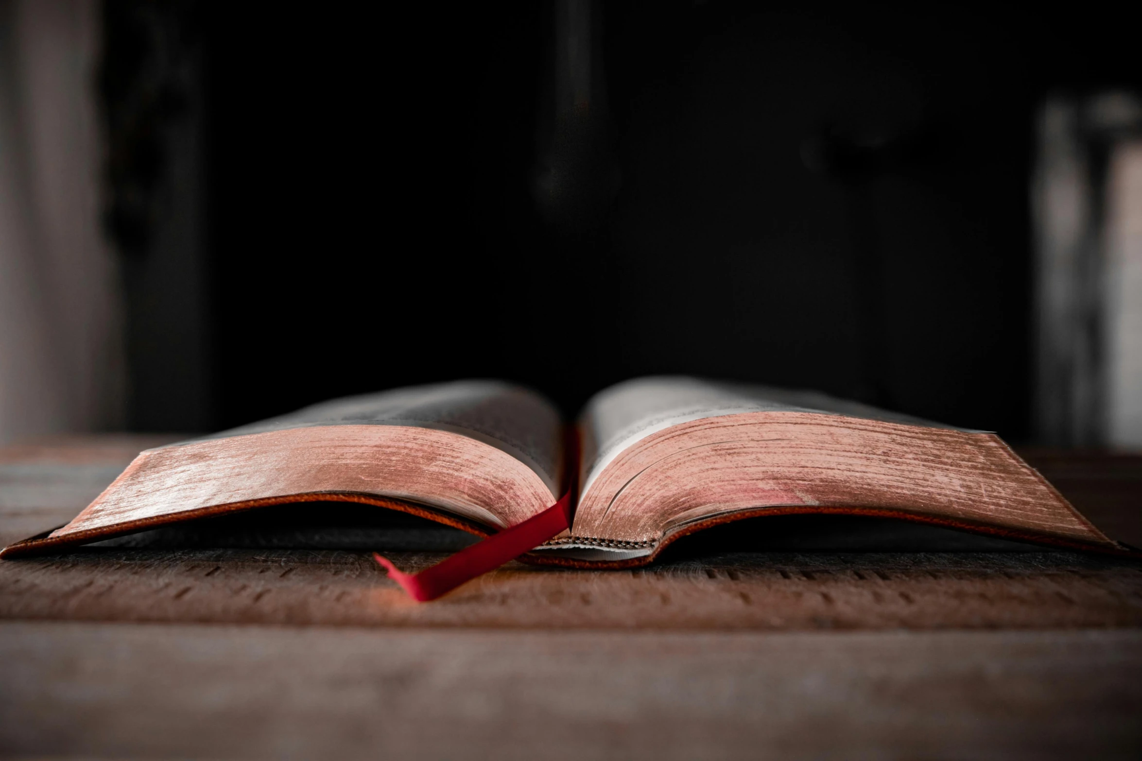 an open book sitting on top of a wooden table, black steel with red trim, thumbnail, religious, dimly lit