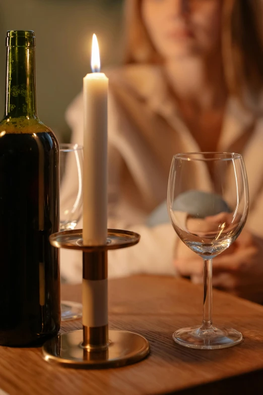 a woman sitting at a table with two wine glasses and a candle, wine bottle, intimate holding close, ambiance