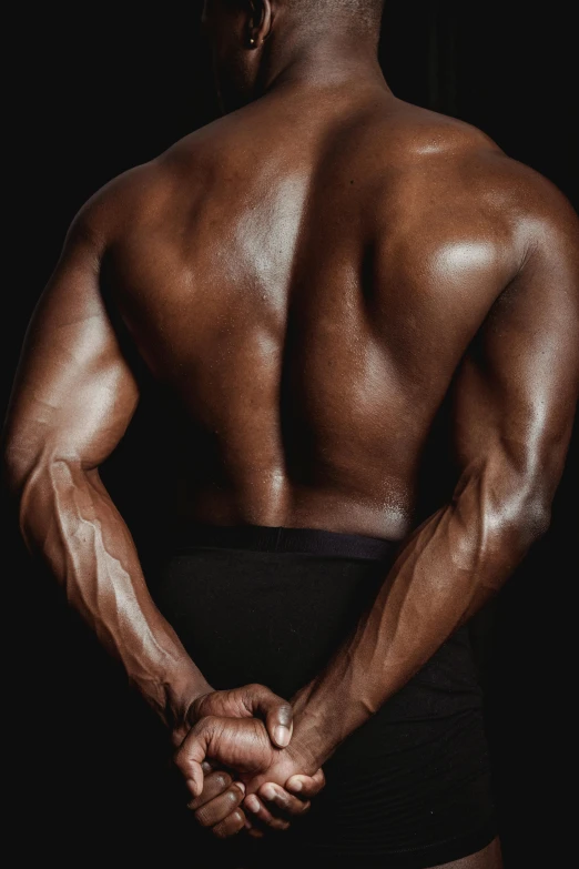 a man standing with his back to the camera, inspired by Terrell James, musclebound and hulking, dark skin tone, closeup of arms, taken in the late 2010s