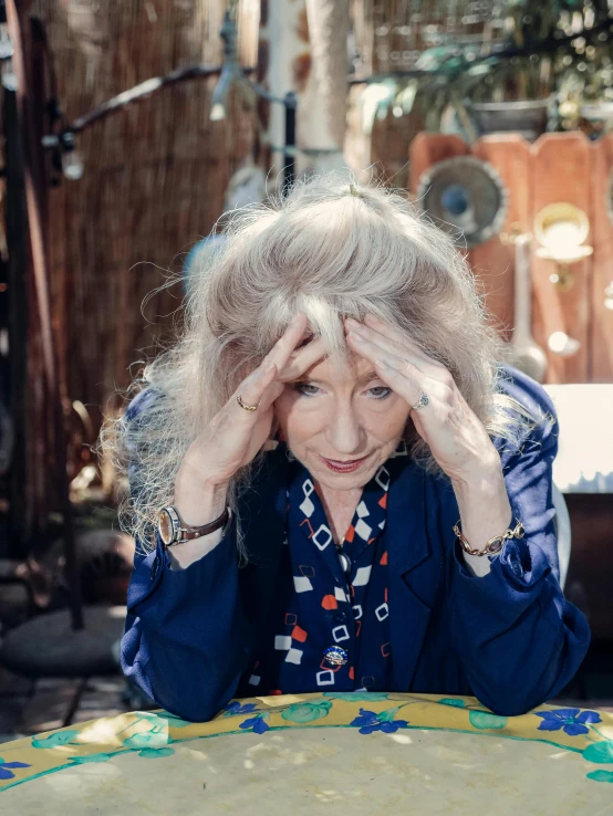 a woman sitting at a table with a cake in front of her, an album cover, trending on unsplash, photorealism, messy wavy white hair, exasperated expression, elderly woman, al fresco