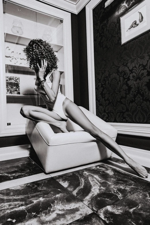 a black and white photo of a woman sitting on a chair, inspired by Helmut Newton, pexels contest winner, curly afro, legs stretched!!! intricate, zendaya, white room