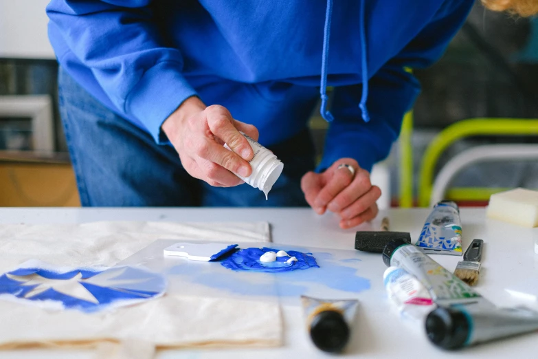 a person putting something in a bottle on a table, inspired by Peter Lanyon, unsplash, process art, blue and white, plastic and fabric, paint tubes, small manufacture