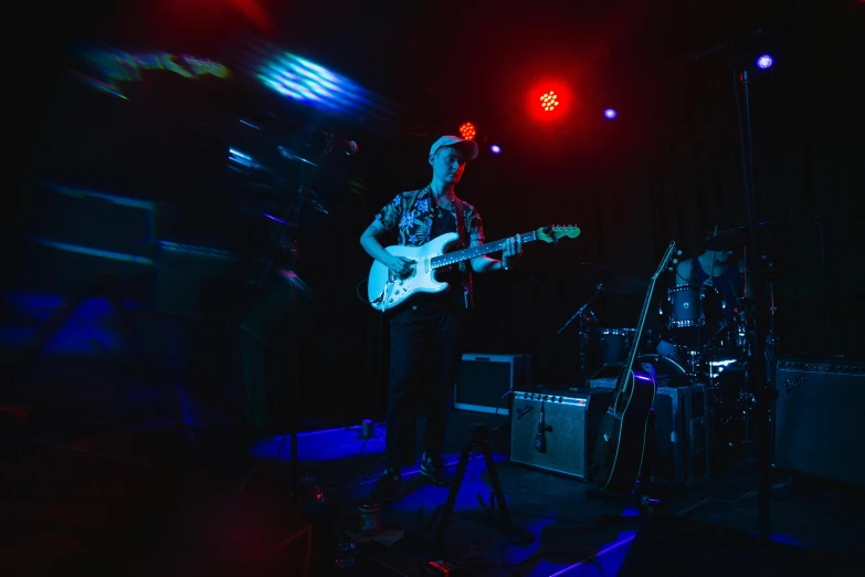 a man that is playing a guitar on a stage, an album cover, unsplash, private press, blue and red lights, group of people in a dark room, slightly overexposed, lachlan bailey