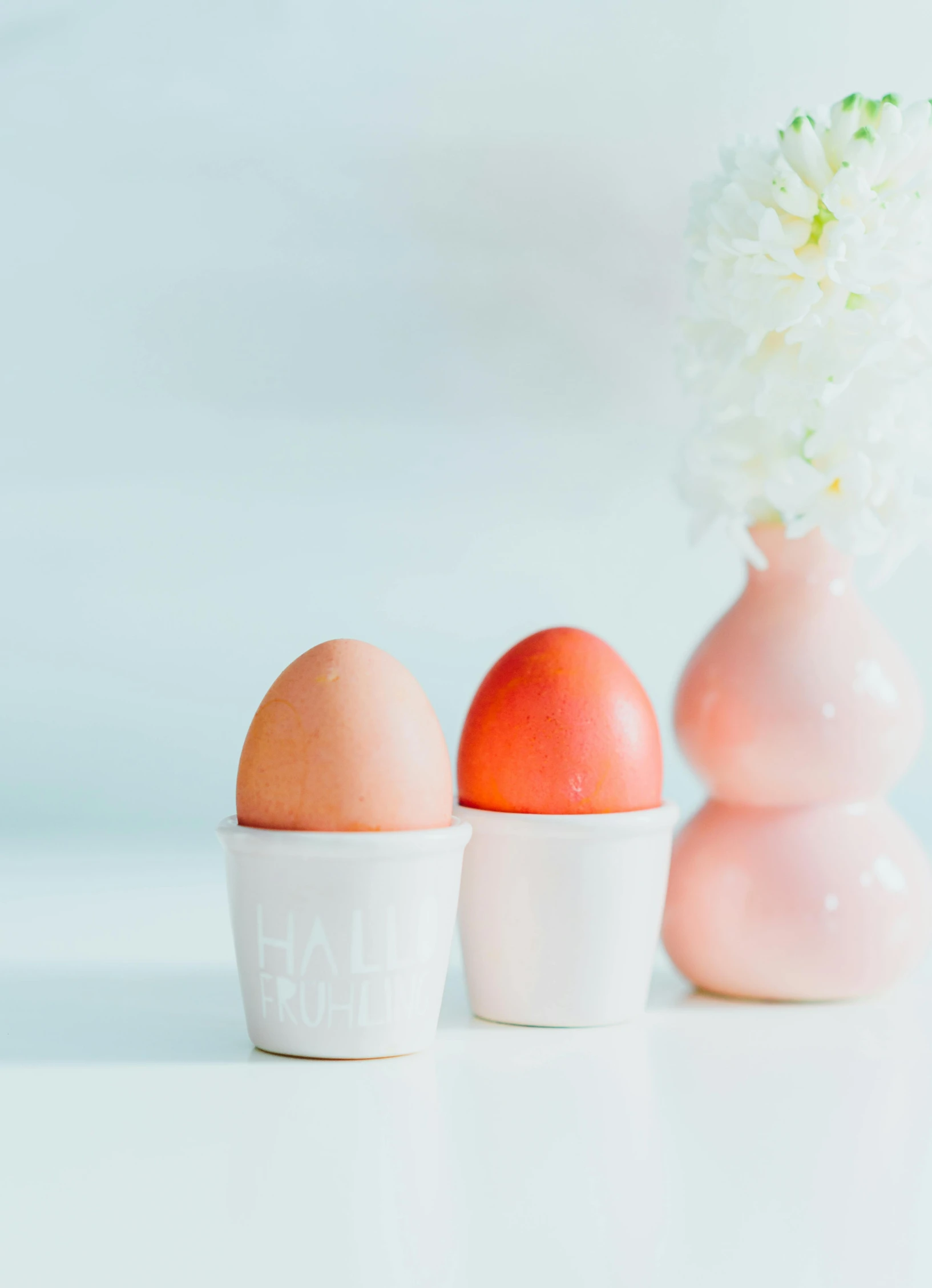 three eggs sitting in a row next to a vase of flowers, inspired by Wilhelm Hammershøi, unsplash, dau-al-set, toned orange and pastel pink, vin diesel head in egg cup, beautifully bright white, pale red