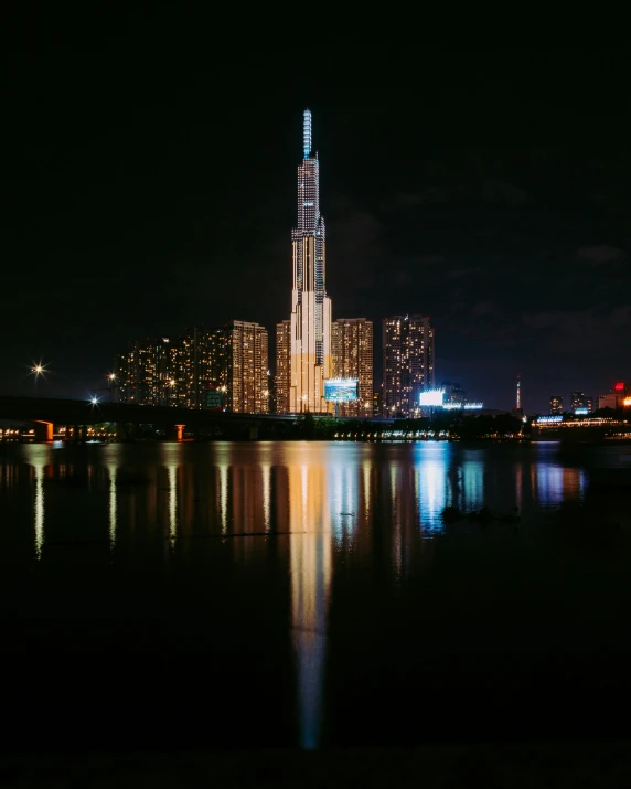 a view of a city at night from across the water, an album cover, by Andrei Kolkoutine, unsplash contest winner, brutalism, gigantic tower, jeongseok lee, taken in the early 2020s, the building is a skyscraper