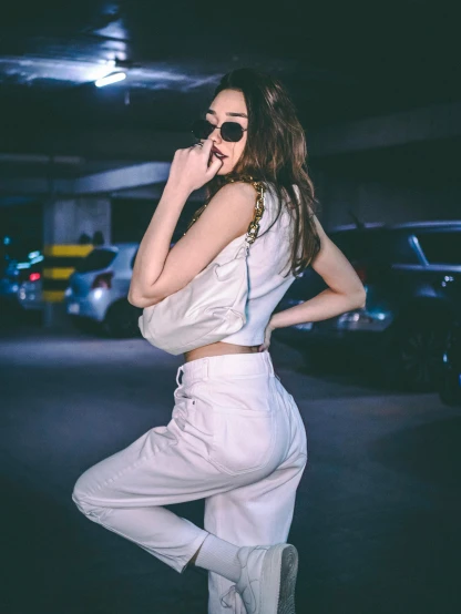 a woman standing in a parking garage talking on a cell phone, inspired by Elsa Bleda, trending on pexels, happening, white pants, belle delphine, sexy pose, baggy pants