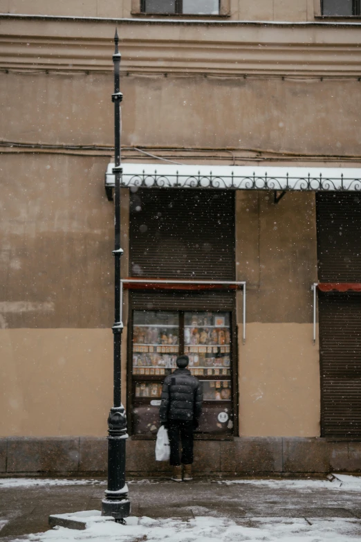 a person standing in front of a store on a snowy day, trending on unsplash, sand - colored walls, bookshops, spanish alleyway, gif