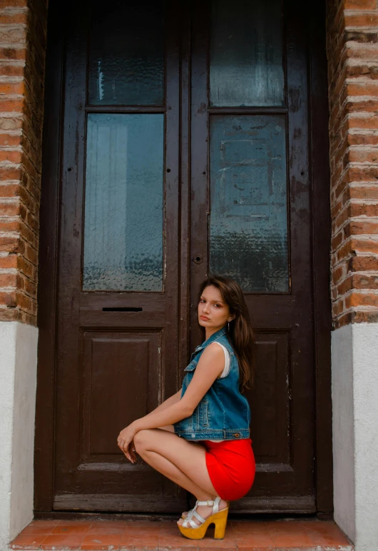 a woman sitting on a step in front of a door, by Julia Pishtar, pexels contest winner, wearing red shorts, brown haired, low quality photo, cool pose