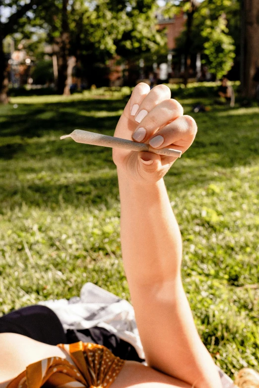 a woman laying in the grass with a knife in her hand, trending on pexels, ganja, long trunk holding a wand, hand gesture, with a long