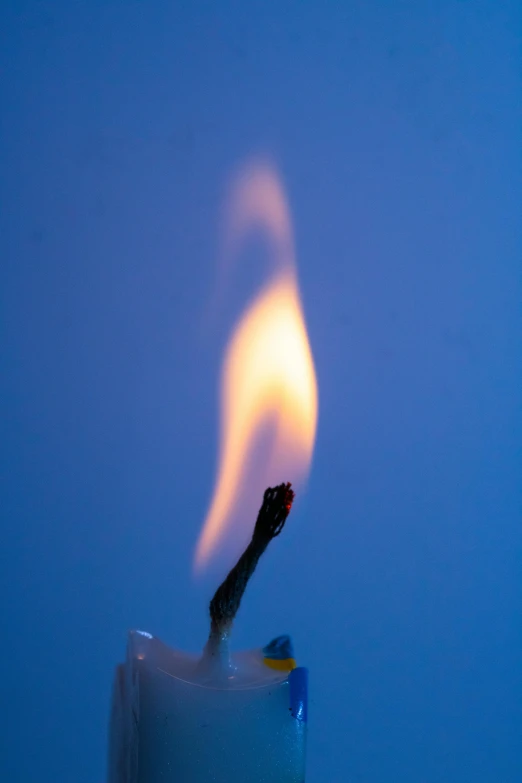 a lit candle in front of a blue background, tiny firespitter, often described as flame-like, photo taken in 2018, burnout