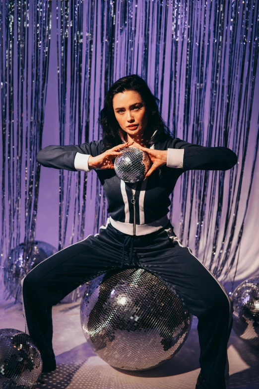 a woman sitting on top of a disco ball, a purple suit jacket, charli bowater, holding a ball, wearing a track suit