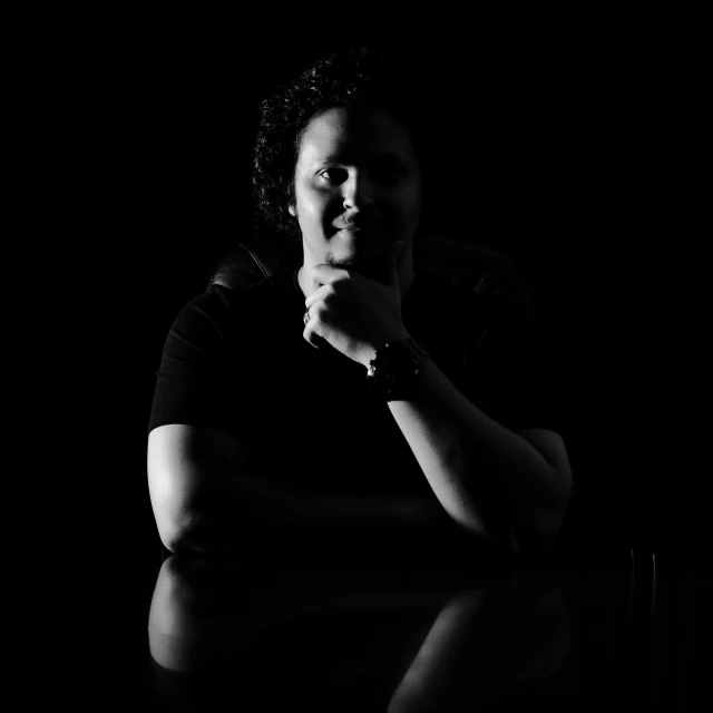 a black and white photo of a man sitting at a table, a black and white photo, unsplash, a portrait of a plump woman, backlight studio lighting, giorgio a. tsoukalos, candid!! dark background