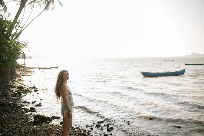 a woman standing on a beach next to a body of water, a picture, morning lighting, kailee mandel, conde nast traveler photo