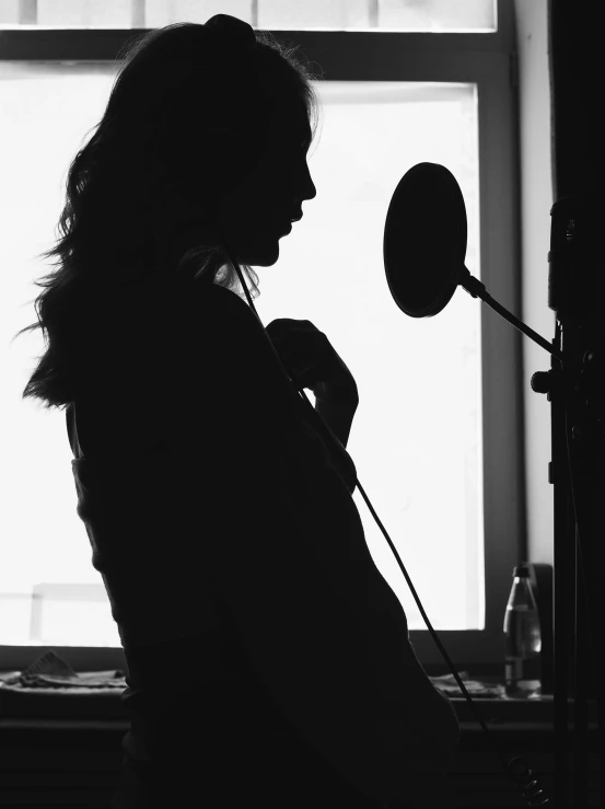 a woman that is standing in front of a window, a black and white photo, by Christen Dalsgaard, unsplash, process art, microphone silluette, putting makeup on, headphone stand, cinematic. by leng jun