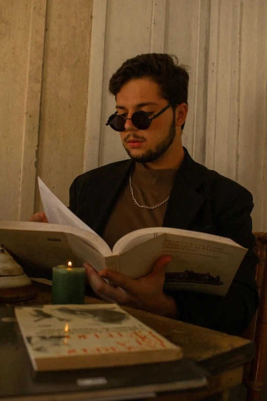 a man sitting at a table reading a book, an album cover, pexels contest winner, young handsome pale roma, ✨🕌🌙, wearing shades, candlelit