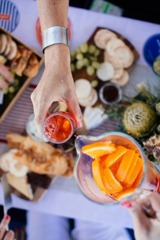 a group of people standing around a table filled with food, holding a glass of wine, orange details, up close, inspiration