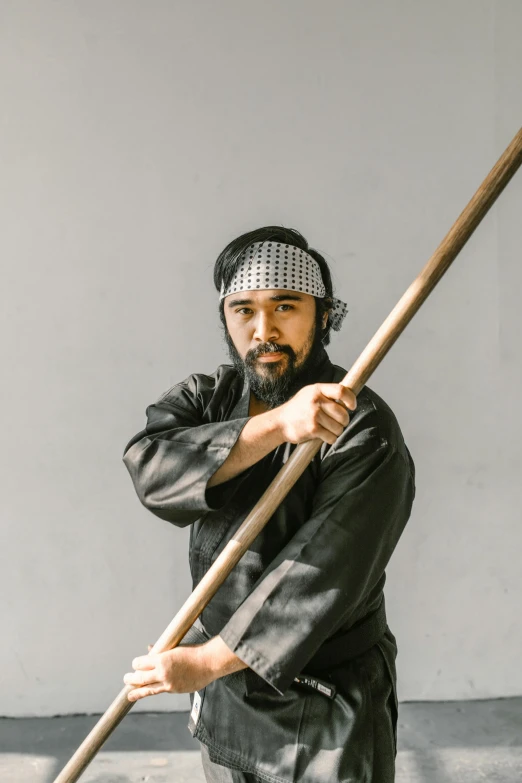 a man in a black outfit holding a wooden stick, inspired by Kanō Hōgai, unsplash, shin hanga, holding scale and holding sword, promotional photo, bao pham, khyzyl saleem