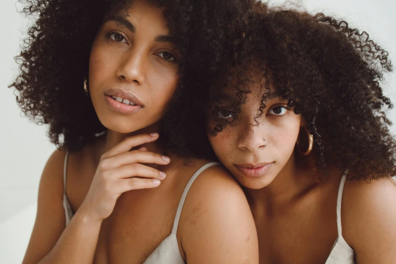 a couple of women sitting next to each other, trending on pexels, renaissance, with textured hair and skin, intimately holding close, looking straight to camera, curls