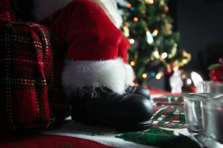 a santa hat sitting on top of a table next to a christmas tree, by Alice Mason, pexels contest winner, leather clothing and boots, very close up foot shot, an elf, tiny feet