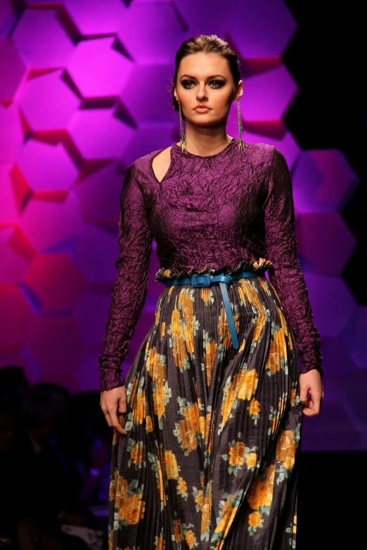 a woman walking down a runway wearing a long skirt, by Gwen Barnard, yellow and purple tones, ritu kumar, deep texture, promo image