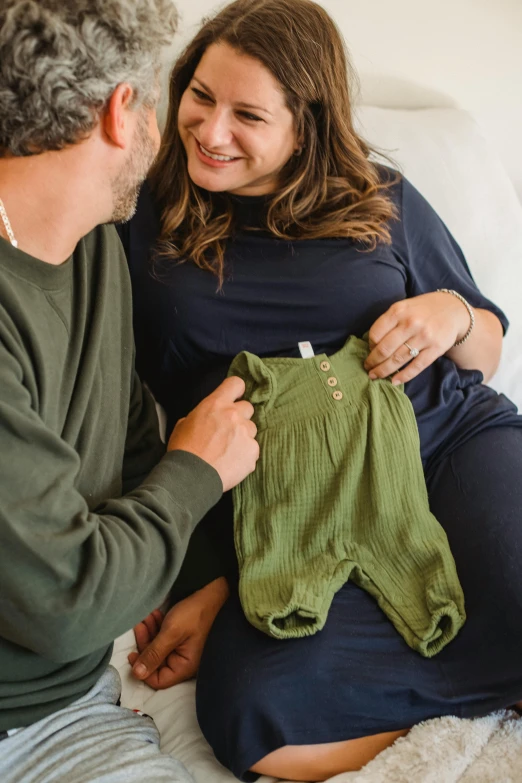 a man sitting next to a pregnant woman on a bed, by Nicolette Macnamara, pexels contest winner, casual green clothing, detailed product shot, belly button showing, little kid