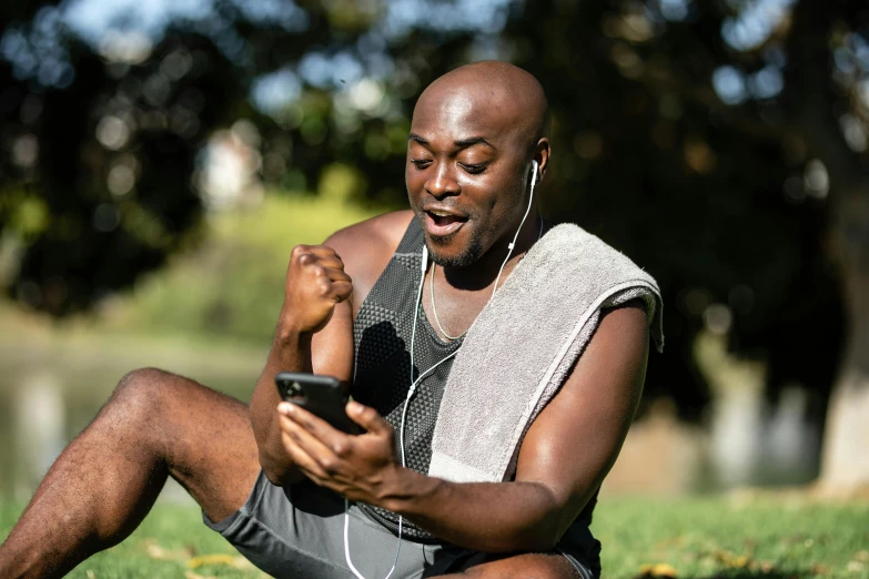 a man sitting on the grass using a cell phone, pexels contest winner, happening, wearing fitness gear, man is with black skin, bald, excitement