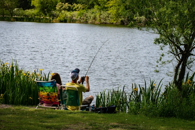 a group of people sitting next to a body of water, people angling at the edge, esher, campsites, parks and lakes