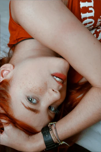 a beautiful young woman laying on top of a bed, inspired by Elsa Bleda, trending on pexels, renaissance, crimson red hair and red eyes, gif, looking from slightly below, low quality photo