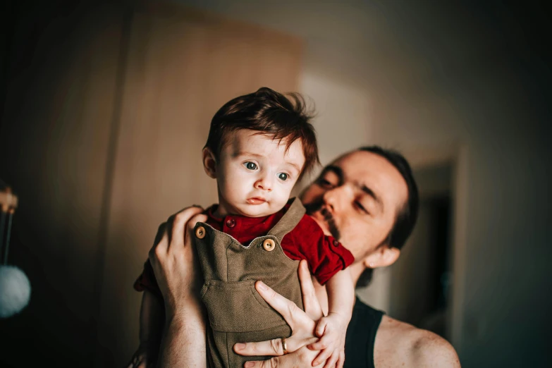 a man holding a baby in his arms, pexels contest winner, avatar image, serious expression, high quality image, thumbnail