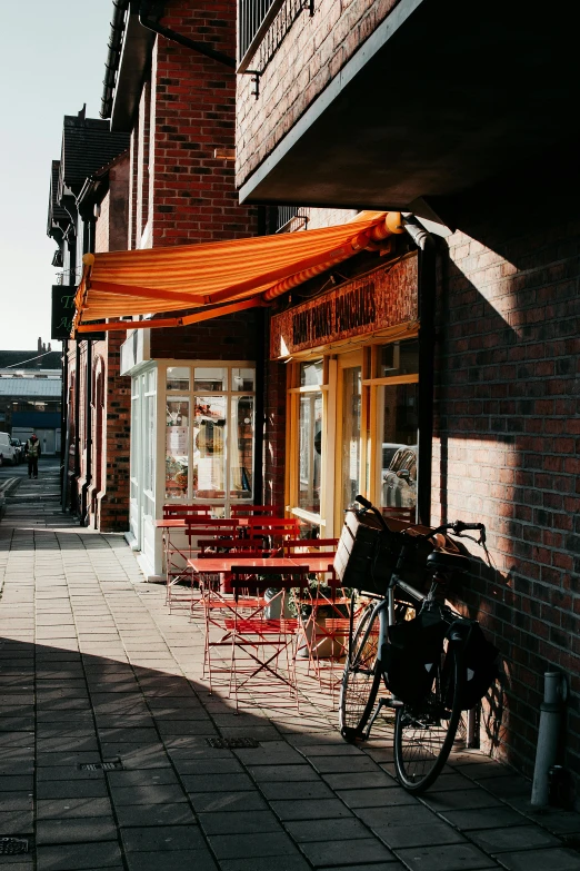 a bicycle parked on the side of a brick building, by Niko Henrichon, unsplash, art nouveau, cafe tables, awnings, swedish urban landscape, orange roof