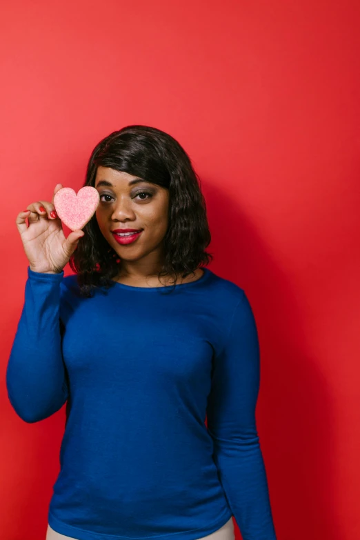 a woman holding a pink heart in front of her face, an album cover, by Arabella Rankin, shutterstock contest winner, blue backdrop, snacks, photo of a black woman, 15081959 21121991 01012000 4k