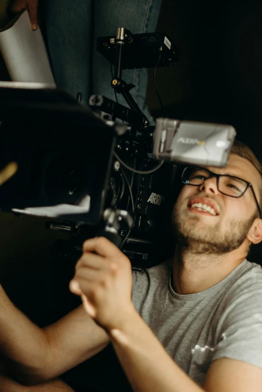 a man that is sitting down with a camera, production quality cinema model, pictured from the shoulders up, lovingly looking at camera, technical