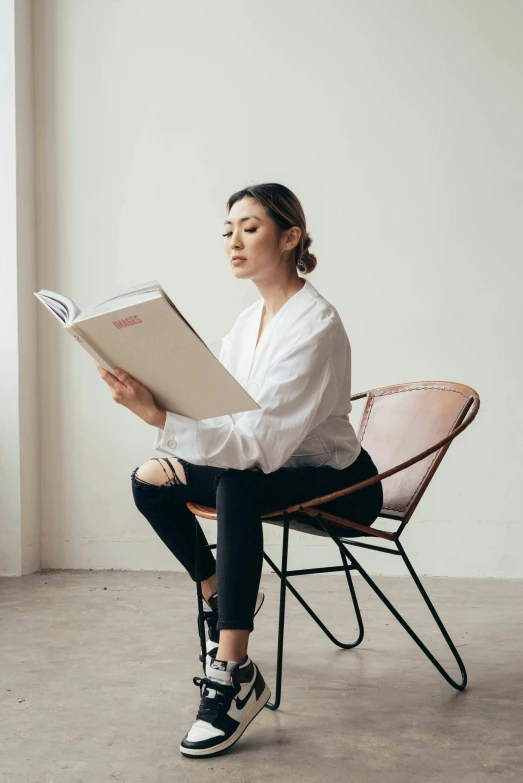 a woman sitting in a chair reading a book, pexels contest winner, minimalism, wearing a white shirt, mahira khan as a d&d wizard, woman in streetwear, cindy avelino