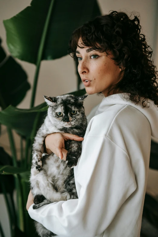 a woman holding a cat in her arms, by Julia Pishtar, trending on unsplash, with long curly, wearing a track suit, gray mottled skin, brunette woman