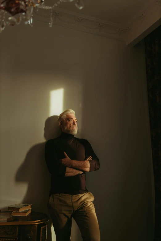 a man standing in a room next to a chandelier, by Attila Meszlenyi, unsplash, photorealism, white hair and white beard, sun flares, thoughtful pose, standing under a beam of light