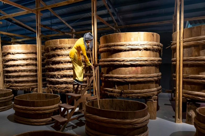 a man standing in a room filled with wooden barrels, inspired by Fu Baoshi, process art, ropes, with yellow cloths, thumbnail, museum quality photo