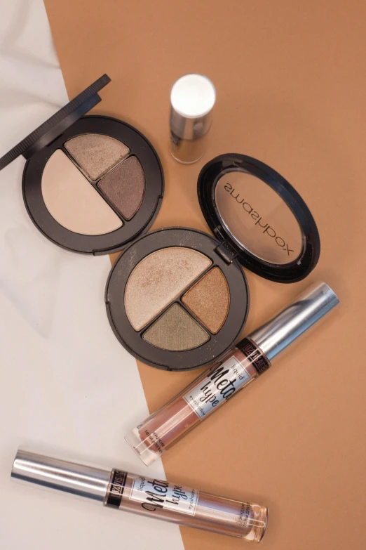 a close up of various cosmetics items on a table, earthtone colors, detailed product image, under a spotlight, wearing eye shadow