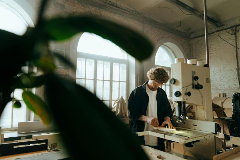 a man standing in front of a sewing machine, by Lee Loughridge, pexels contest winner, arts and crafts movement, big windows, plants, lachlan bailey, working in the forge