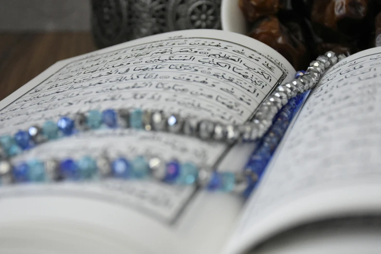 an open book sitting on top of a wooden table, by Sheikh Hamdullah, hurufiyya, blue and silver, beads, a close up shot, photograph credit: ap