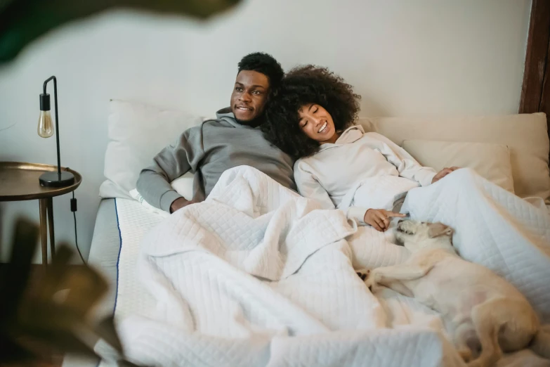 a man and woman laying in bed next to each other, by Carey Morris, pexels contest winner, sitting on couch, african american, having a good time, wearing simple robes